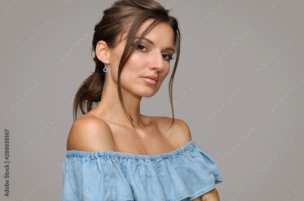 Beautiful young woman with bare shoulders with a beautiful professional evening make-up and hairstyle in a blue top with ruffles. Beautiful young woman with bare shoulders with a beautiful professional evening make-up and hairstyle in a blue top with ruffles.