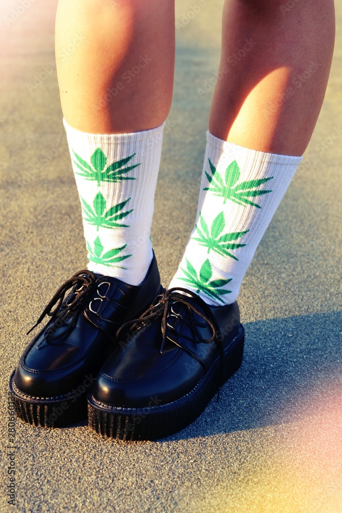 Black sneakers and high white socks with marijuana prints dressed on girl's legs.