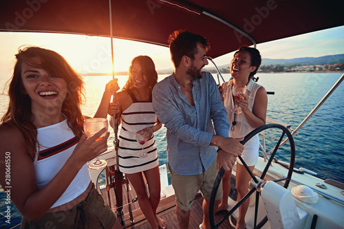 Happy friends sailing on the luxury boat together drink wine and have party at sunset. .