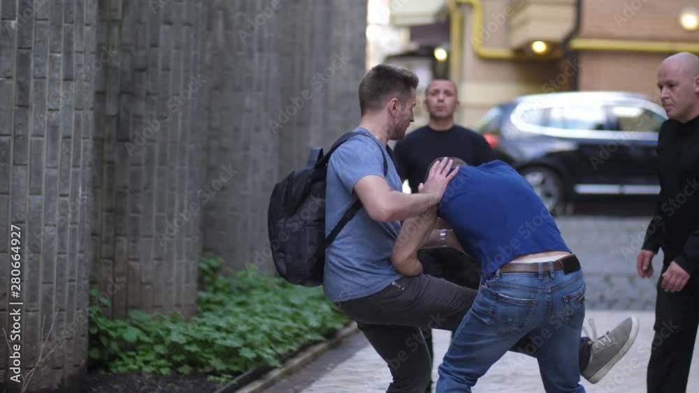 Close-up of armed criminals attacking male walking in city street. Fearless man knocking three muggers applying Krav Maga self defence and running away Close-up of armed criminals attacking male walking in city street. Fearless man knocking three muggers applying Krav Maga self defence and running away