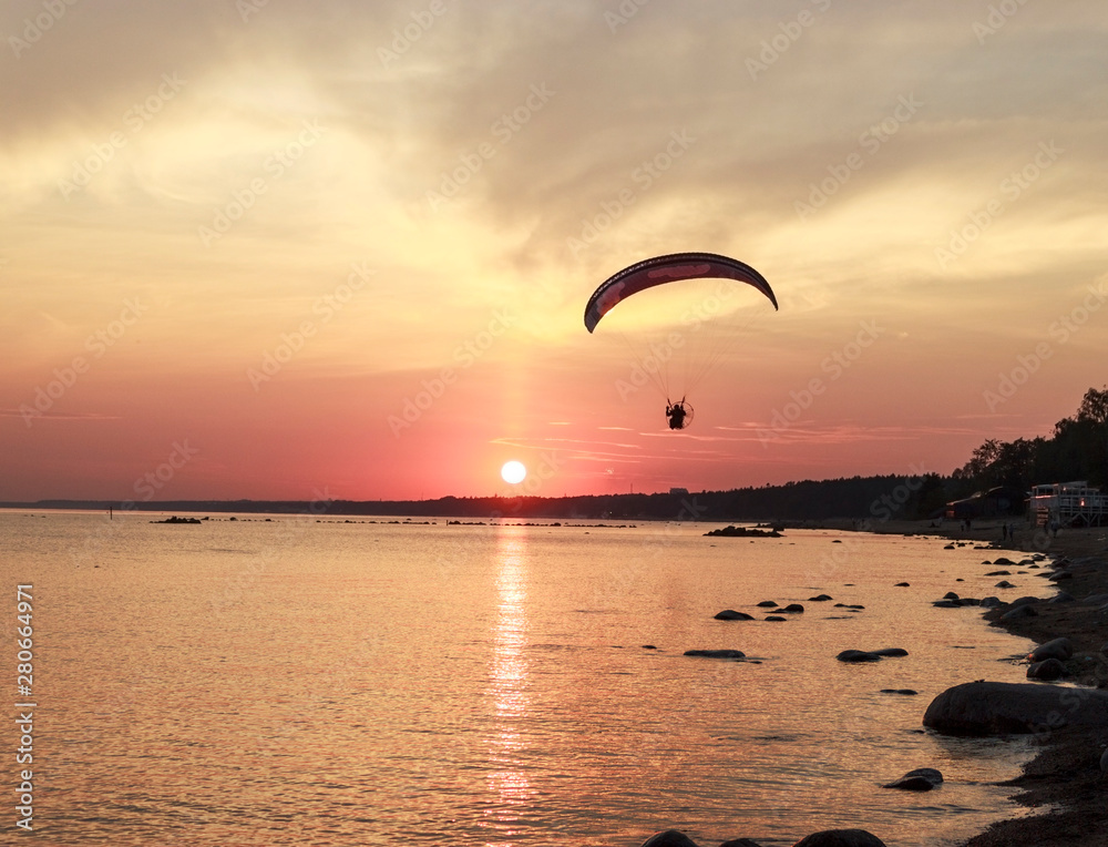 Sunset over the sea. Reflection of the sun in water. Silhouette of paraglider flying in the sky. Sunset beach in a summer evening. Gulf of Finland, Baltic sea, Komarovo, Saint-Petersburg, Russia. Sunset over the sea. Reflection of the sun in water. Silhouette of paraglider flying in the sky. Sunset beach in a summer evening. Gulf of Finland, Baltic sea, Komarovo, Saint-Petersburg, Russia.