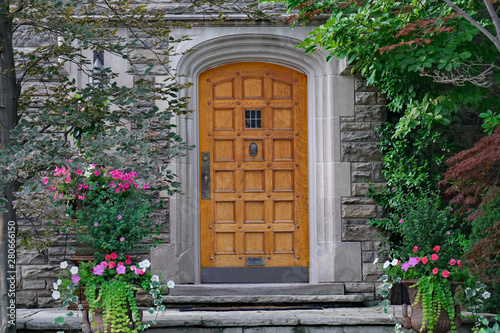 elegant wooden front door of stone house surrounded by summer flowers and trees