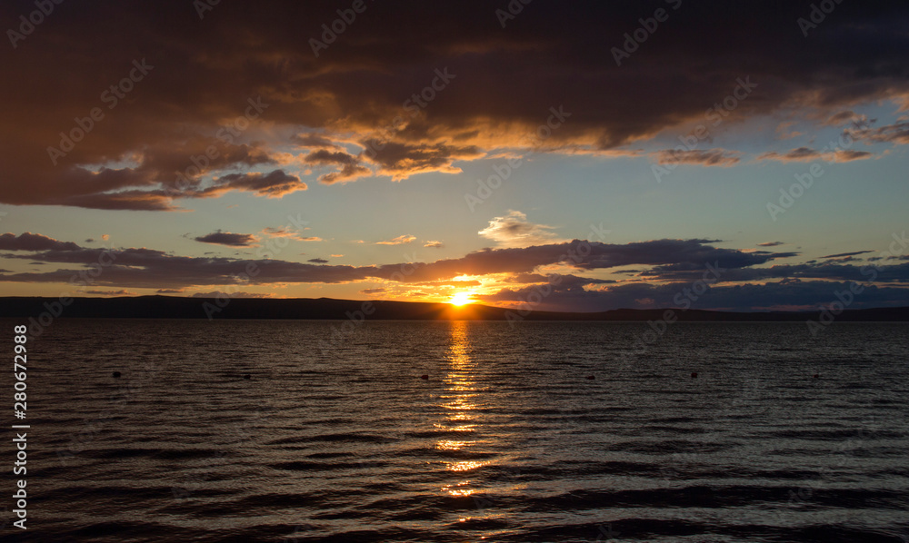 sunset, dramatic clouds, reflection of the sun in the water of the lake