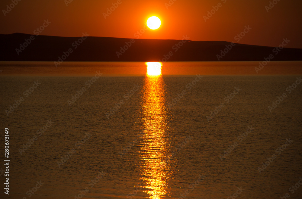 Beautiful golden orange sunset over the lake. The sun sets turning the sky yellow, orange & red tones & reflects in the lake.