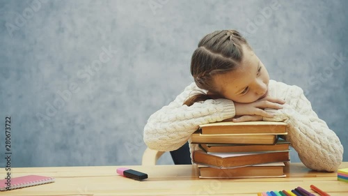 Sleepy little girl folded her hands over a stack of books.