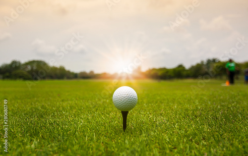 Golf ball on tee ready to shot on blurred landscape of green course with sunlight on background. photo