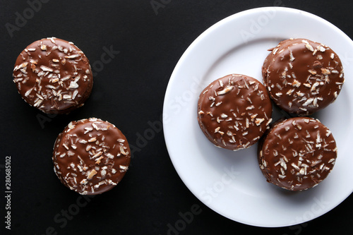 Chocolate cookies with coconut shaving chocolate coating and coconut on wooden black  background.