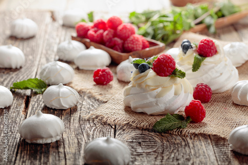Dessert Pavlova with raspberries, blueberries and mint on a old wooden table.