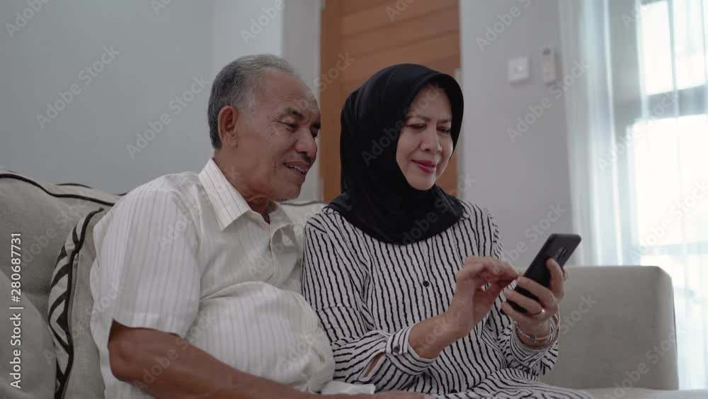happy senior muslim couple using mobile phone in living room. old asian people