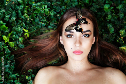 Portrait of beautiful young girl with butterfly sitting on her face. Big black butterfly Papilio lowi sat on the woman's forehead. Asymmetrical position