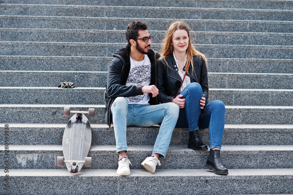 Cool multiracial couple sitting on stairs with longboard. Cool multiracial couple sitting on stairs with longboard.