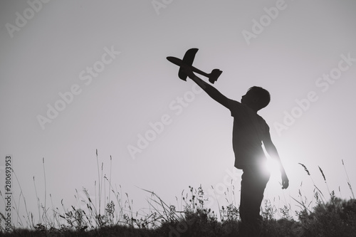 Black and white horizontal image of cute happy kid playing outside with toys. Boy standing in beautiful sunny sunset landscape.