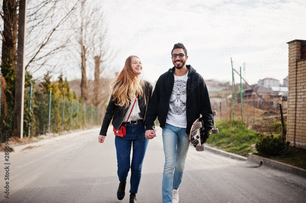 Cool multiracial couple walking together with longboard.