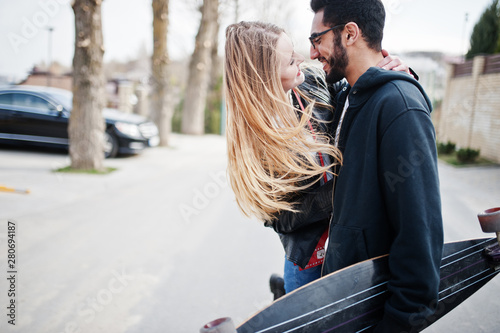 Cool multiracial couple walking together with longboard. photo