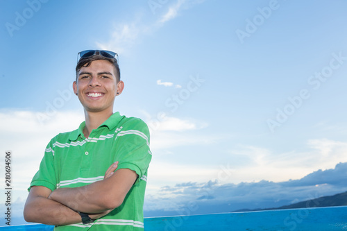 Young guy portrait outdoors. He has his arms crossed and is smiling to the camera.