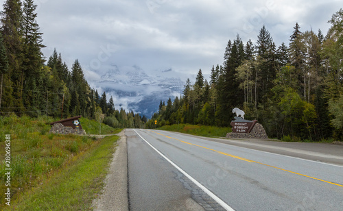 Road into the Canadian Rockies with Mount Robson in the background covered with fog and the Mount Robson Provincial Park sign beside the road