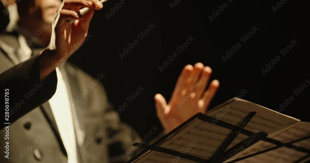 Male orchestra conductor controlling music in orchestra pit by movement of his hands and white baton, studio shot on black background 4k footage
