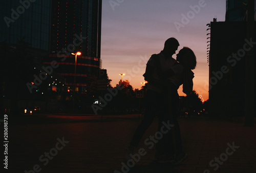 Silhouette of young happy couple in love dancing on city street at sunset