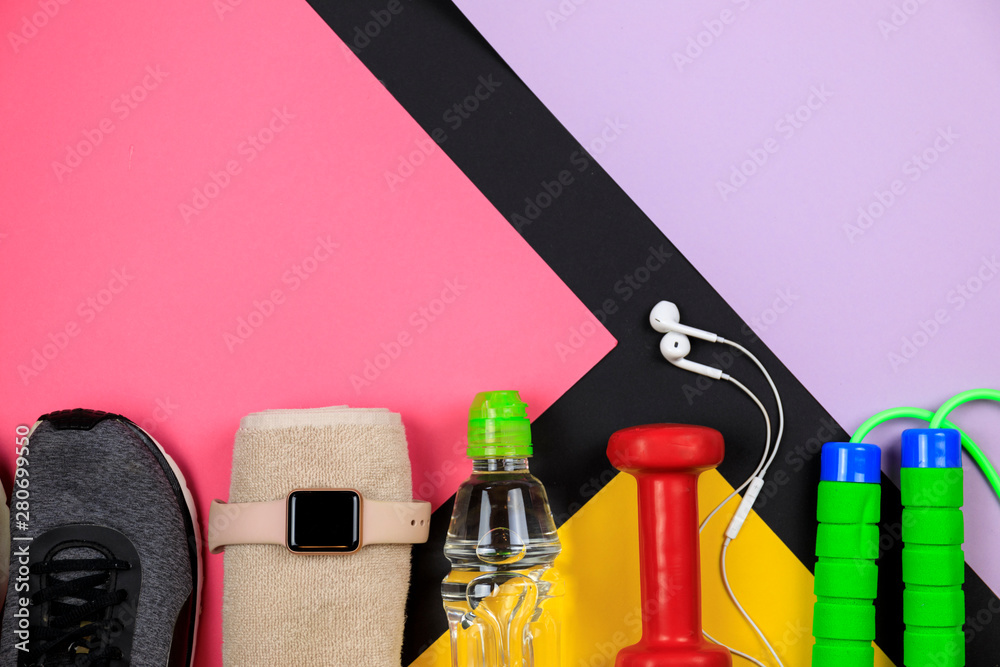 Sports equipment for fitness training on a color background. Bottle with water, smart watch, earphones and jumping-rope. Set for sports activities.