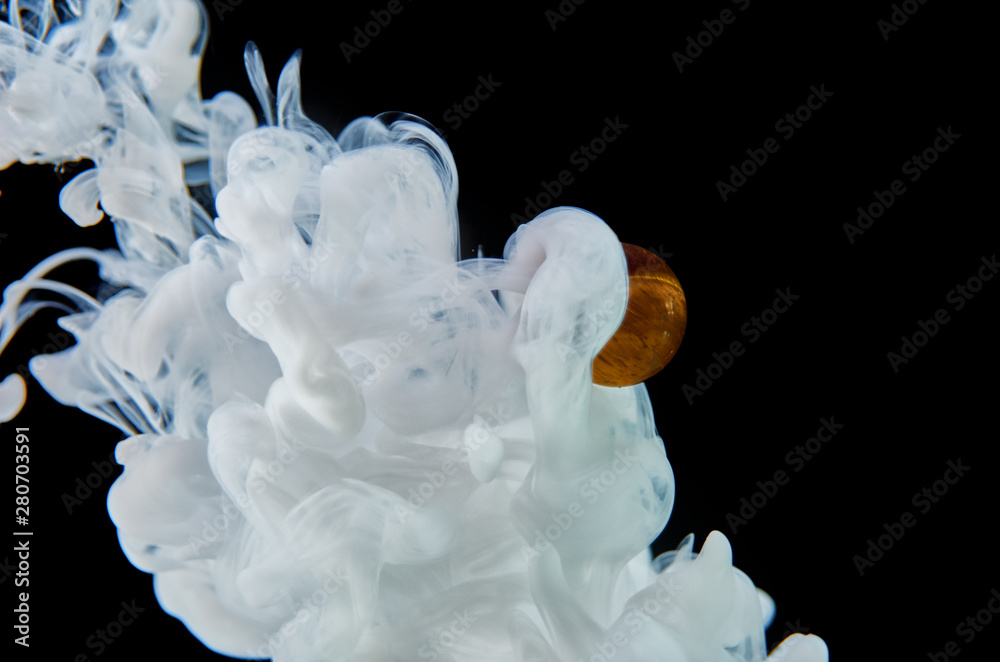 White acrylic ink in water on a black background surrounds the glass ball. Abstract background. White acrylic ink in water on a black background surrounds the glass ball. Abstract background.