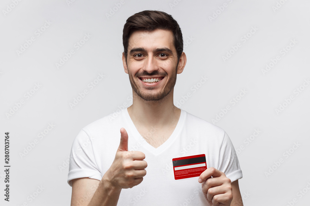 Happy man holding credit card and showing thumbs up gesture if recommend the best bank, isolated on gray background Happy man holding credit card and showing thumbs up gesture if recommend the best bank, isolated on gray background