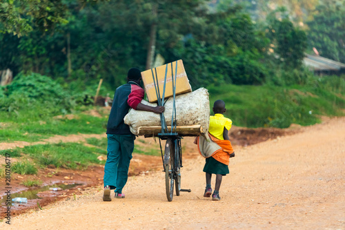 A ugandan man and a child transporting things with a bicycle
