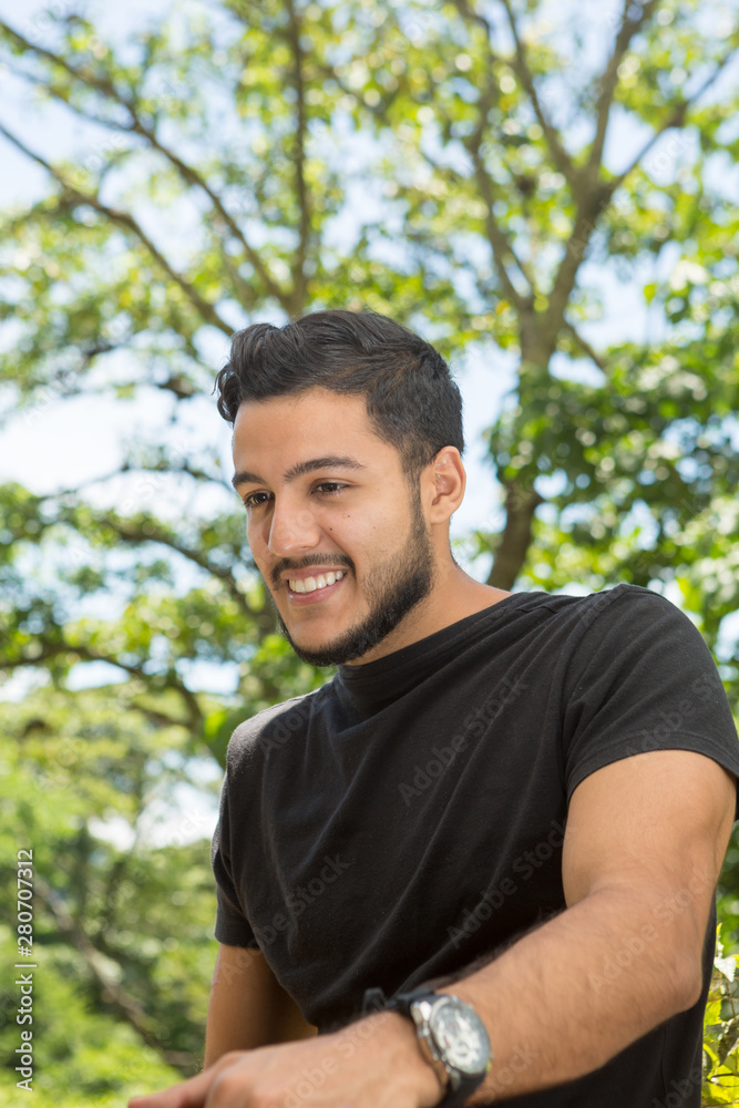 Young latin man portrait indoors next to a window with nature as background. He is smiling. Young latin man portrait indoors next to a window with nature as background. He is smiling.