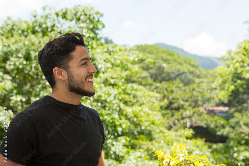 Young latin man profile portrait indoors next to a window with nature as background. He is smiling. Young latin man profile portrait indoors next to a window with nature as background. He is smiling.