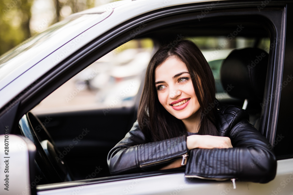 Beautiful girl in jacket is smiling while driving a car