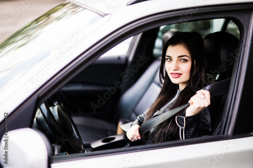 Young elegant woman putting on safety belt in her car