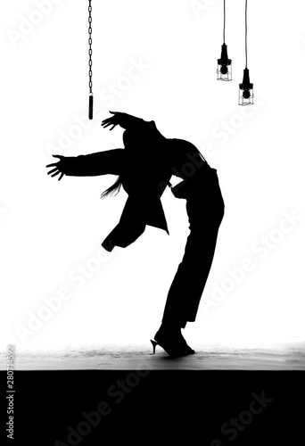 A female dancer dances on an old worn out stage. Dressed in men's clothing, she is seen dancing as a silhouette.