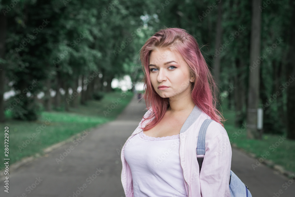 Attractive young woman in plaid shirt holding backpack while standing in the city park Attractive young woman in plaid shirt holding backpack while standing in the city park