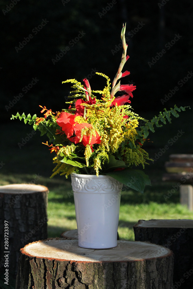 Bouquet of red and yellow flowers and fern leaves in a white pot.