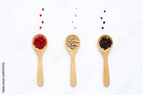 Black, red and white peppercorns with wooden spoon on white