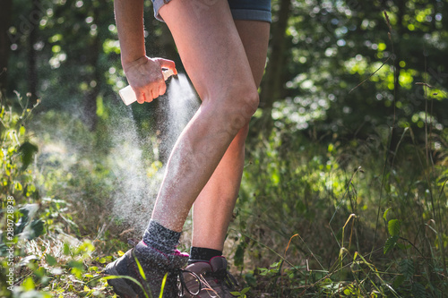 Insect repellent. Woman applying mosquito repellent on her legs in forest