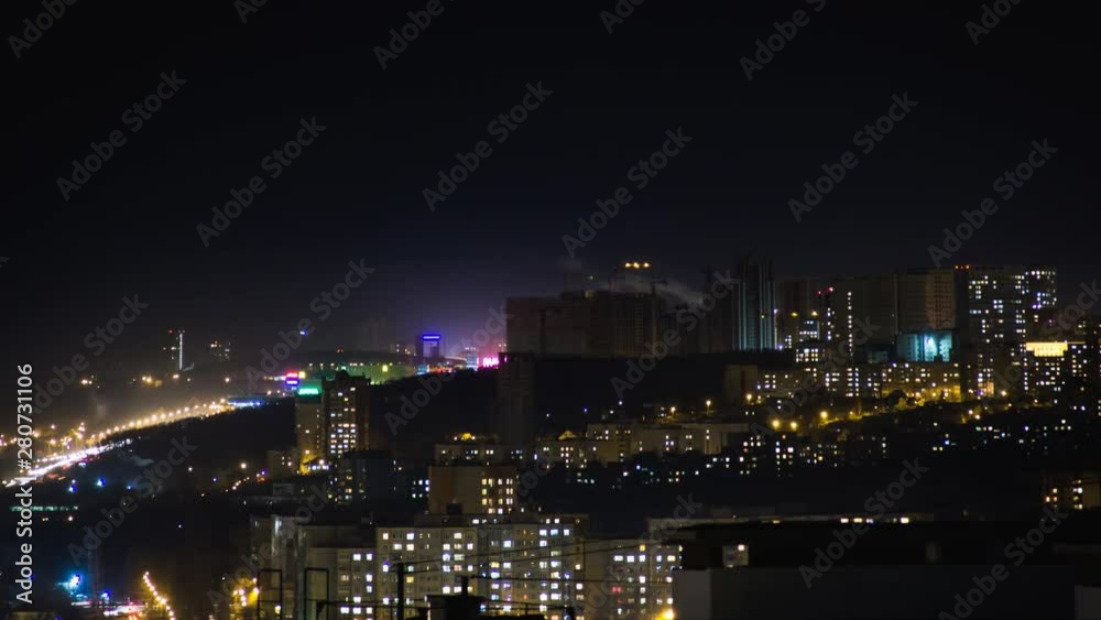 Night city skyline timelapse.Top aerial panoramic view of modern city from tower rooftop. Road junction traffic. Lights flicker in windows.Residential flats of dormitory area close to industrial zone Night city skyline timelapse.Top aerial panoramic view of modern city from tower rooftop. Road junction traffic. Lights flicker in windows.Residential flats of dormitory area close to industrial zone