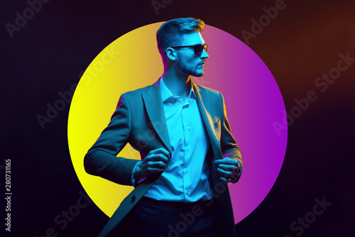 Young handsome model posing in a studio in a trendy neon light. Fashionable man in a stylish suit. Vibrant color. Bright colorful light effects. Disco style. Overlay. Gel filter. Supersaturated