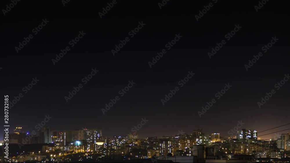 Night city skyline timelapse. Top aerial panoramic view of modern city from tower rooftop. Lights flicker in windows. Stars move on the dark sky.