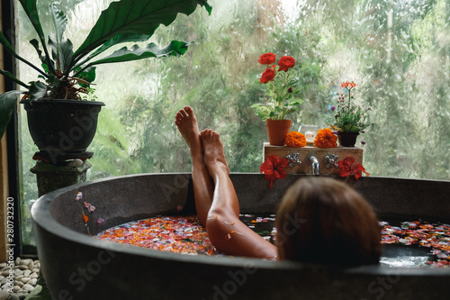 Stampa su tela Back view woman relaxing in round outdoor bath with tropical flowers, organic skin care, luxury spa hotel, lifestyle photo