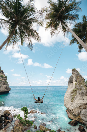 Young girl swinging on a swing overlooking the blue sea. Travel adventure on paradise tropical island. A young girl swinging on a swing between palm trees on the beach of a tropical island