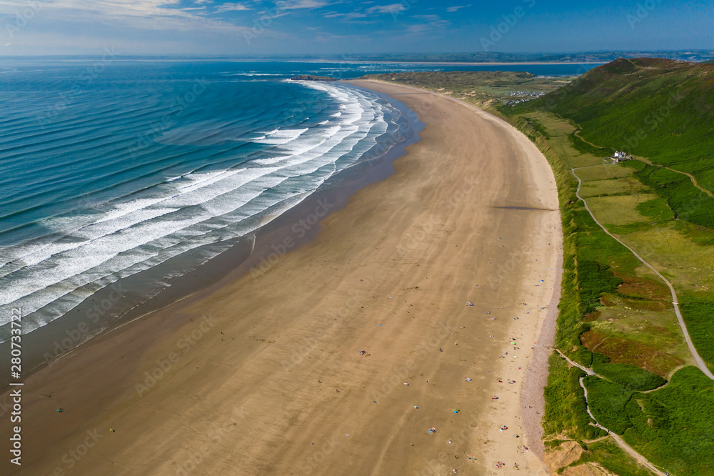 Aerial view of the huge sandy beach and green hills in Rhossili, Swansea