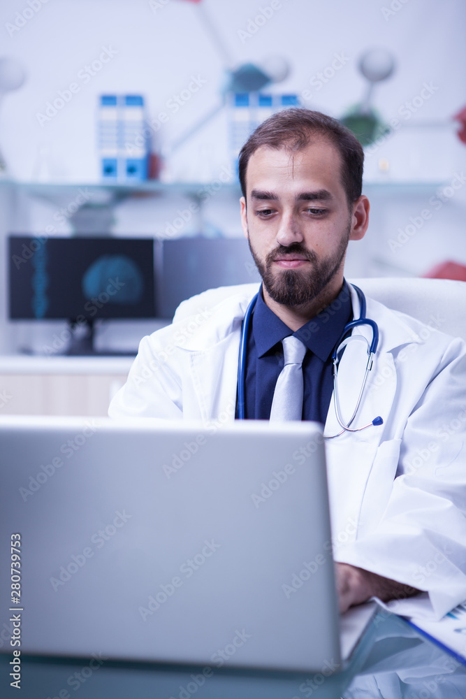Young doctor thinking and working on his laptop in a private laboratory Young doctor thinking and working on his laptop in a private laboratory