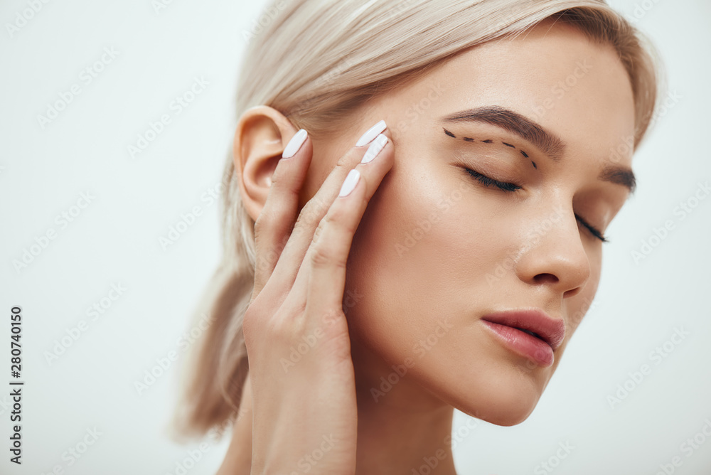 Plastic surgery. Beautiful young blonde woman keeping eyes closed and touching her face with sketch on it Plastic surgery. Beautiful young blonde woman keeping eyes closed and touching her face with sketch on it