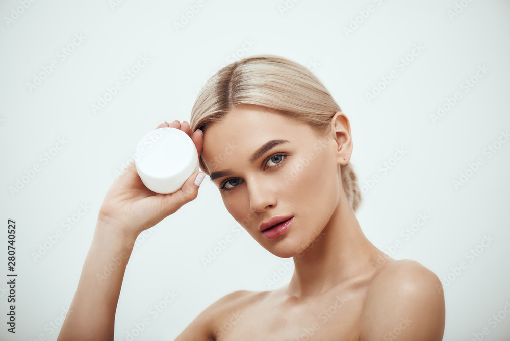 Best Facial Cream. Portrait of gorgeous young blonde woman showing face cream while standing against grey background. Skin care Best Facial Cream. Portrait of gorgeous young blonde woman showing face cream while standing against grey background. Skin care