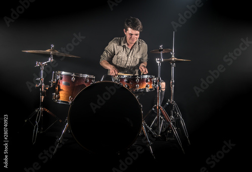 Professional drummer playing on drum set on stage on the black background