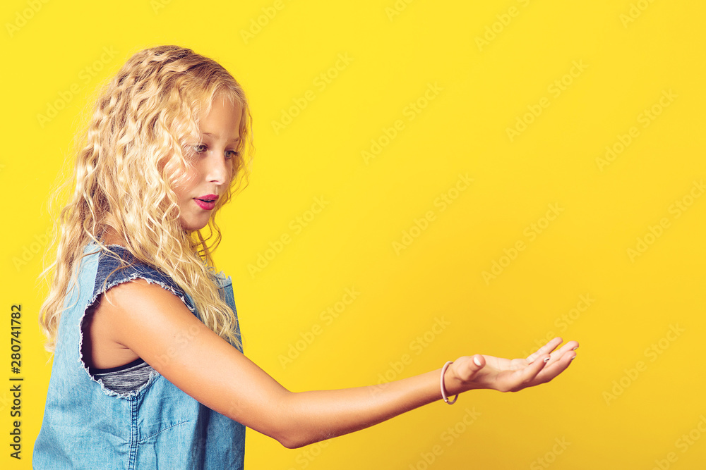 Pretty girl promoting product for kids. Beauty and kids fashion. Healthy hair care. Girl demonstrate product. Product presentation. Profile of happy schoolgirl over yellow background with copyspace Pretty girl promoting product for kids. Beauty and kids fashion. Healthy hair care. Girl demonstrate product. Product presentation. Profile of happy schoolgirl over yellow background with copyspace