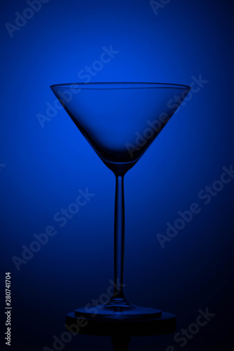 Empty tall martini glass on a black and blue background