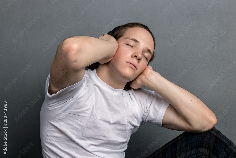 Handsome young man sitting on the floor in living room, having headphones on his head and listening music Handsome young man sitting on the floor in living room, having headphones on his head and listening music