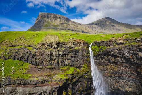 Aerial view of Mulafossur waterfall in Gasadalur village in Faroe Islands, North Atlantic Ocean. Photo made by drone from above. Nordic Natural Landscape.