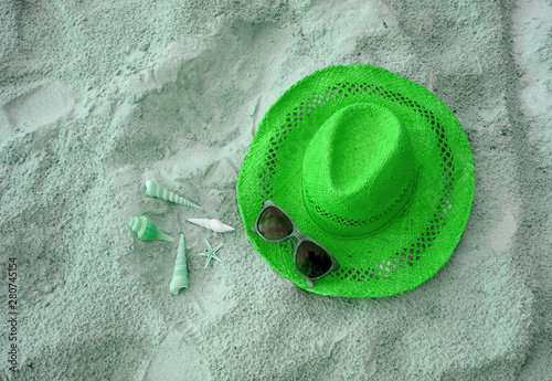 Pop art styled straw hat with many types of little seashells and sunglasses on the sandy beach in green color tone 